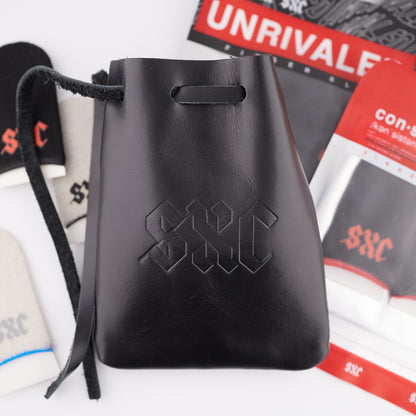Black SXC leather drawstring pouch in front of SXC finger sleeves and product packaging on a white studio background.